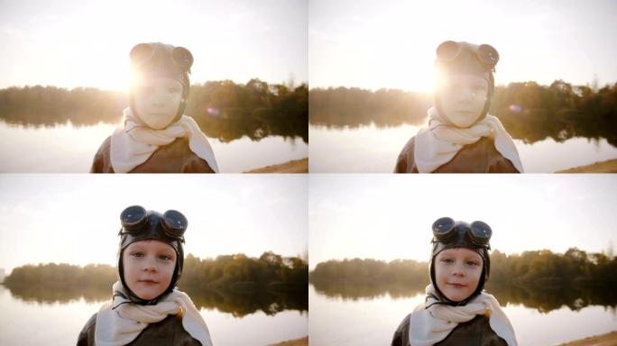 穿着复古飞行员服装的小飞行员男孩，戴着围巾和眼镜，看着相机在日落湖慢动作中微笑。