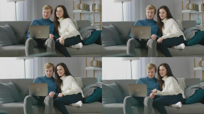 可爱的年轻夫妇使用笔记本电脑，玩得开心，笑，而坐在舒适的公寓的沙发上。夫妇在互联网上购物，使用社交媒