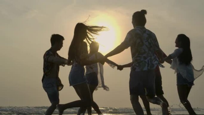 日落时，一群快乐的朋友在海滩派对上在水中玩耍。有旅行、度假和派对概念的人。慢动作。
