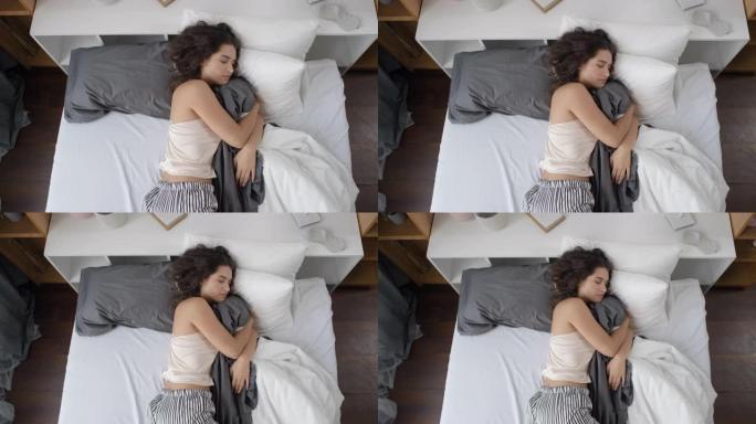 年轻女子侧睡并在床上拥抱毯子的俯视图