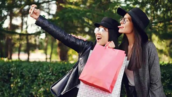开朗的年轻女士购物狂在街上自拍，拿着包，做鬼脸。女人穿着时髦的衣服和眼镜。