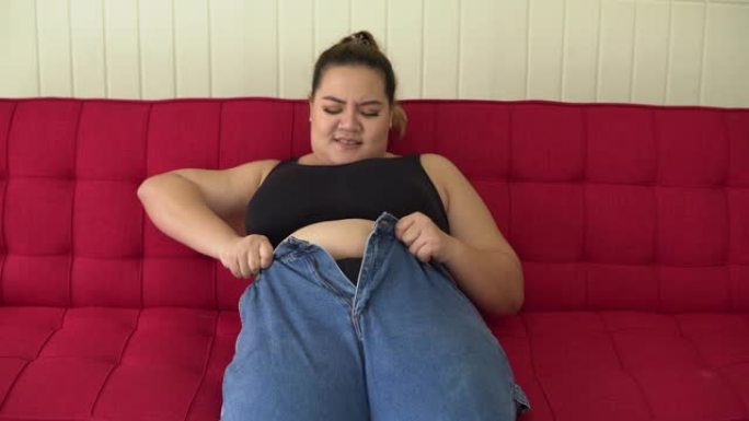 肥胖的女人试图关闭牛仔裤的纽扣