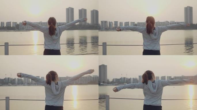 年轻女子张开双臂，看着城市的日落。