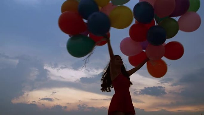 一个飞行的年轻女孩的剪影，气球在日落时蓝天的背景下。