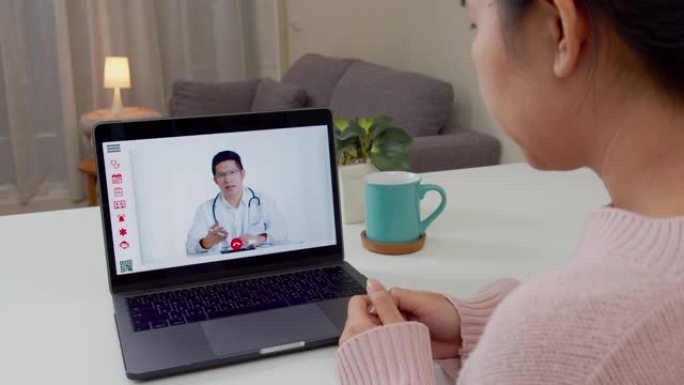 亚洲女性在家与亚洲医生视频通话的后视图。病人女孩咨询与全科医生在电脑笔记本电脑上的应用。医生和顾问在