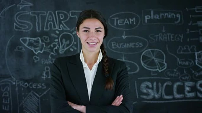 美丽的商业女孩，营销老师，在黑色背景上在黑板上绘制成功图。