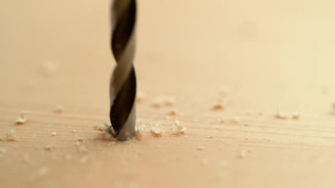 宏观: 木屑和锯末从钻入木板的金属钻头上飞出。