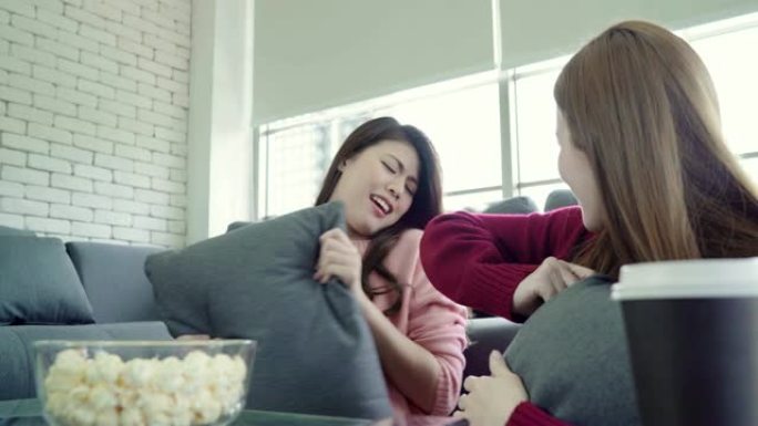 亚洲女性在家里的客厅玩枕头大战和吃爆米花，一群室友朋友躺在沙发上享受有趣的时刻。生活方式女性在家放松