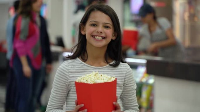 电影院里美丽的小女孩拿着爆米花盒子对着镜头微笑