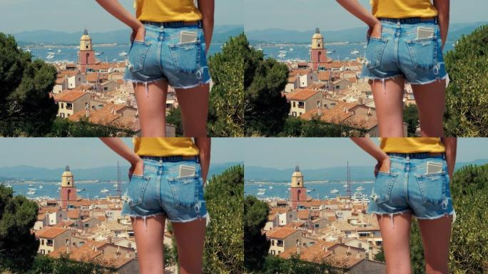 年轻女子穿着牛仔短裤，背景为圣特罗佩老城