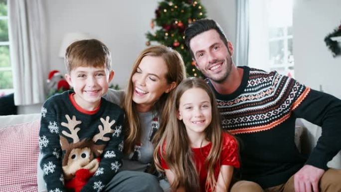 圣诞节那天有孩子穿着节日套头衫的父母的肖像坐在家里休息室的沙发上