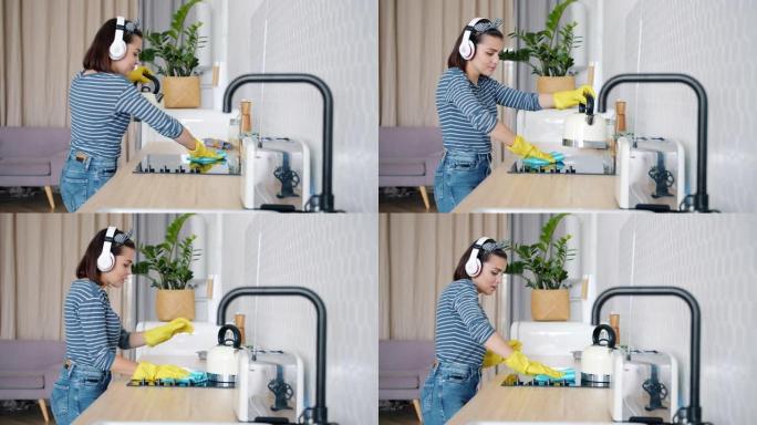 年轻女士的慢动作清洁厨房和耳机听音乐