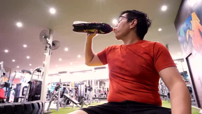 疲惫的大体健男子在健身房喝软饮料汽水。