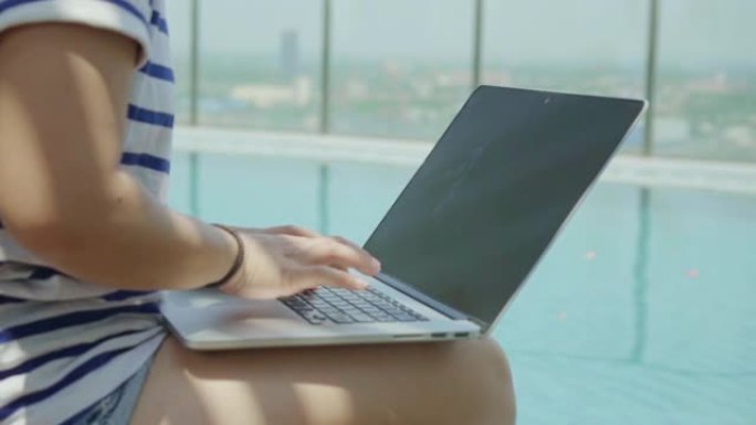 妇女使用笔记本电脑坐在游泳池附近，慢动作