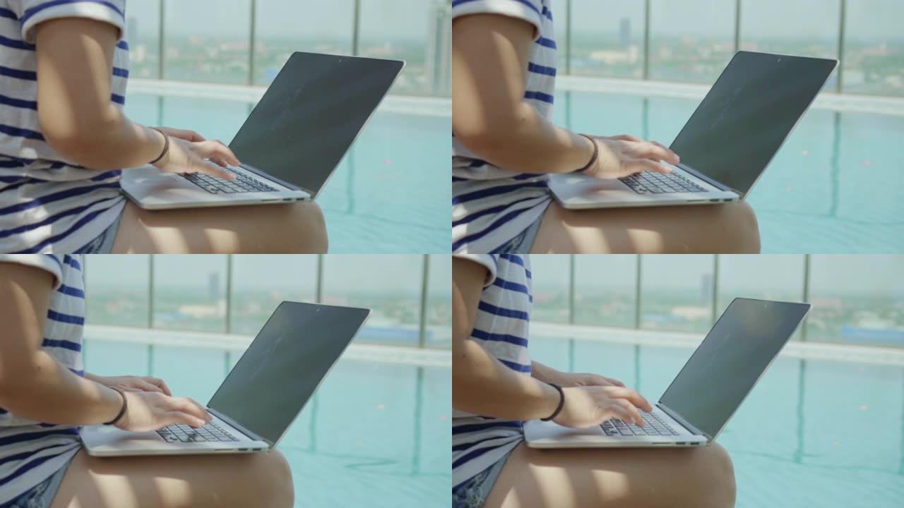 妇女使用笔记本电脑坐在游泳池附近，慢动作