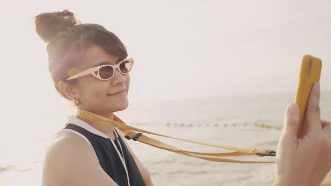 快乐亚洲女人海滩与日落海滩在社交媒体上自拍。