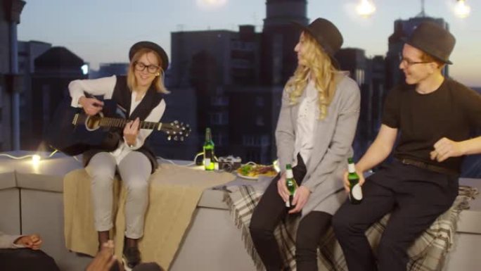 女人在屋顶的夜间聚会上为朋友弹吉他