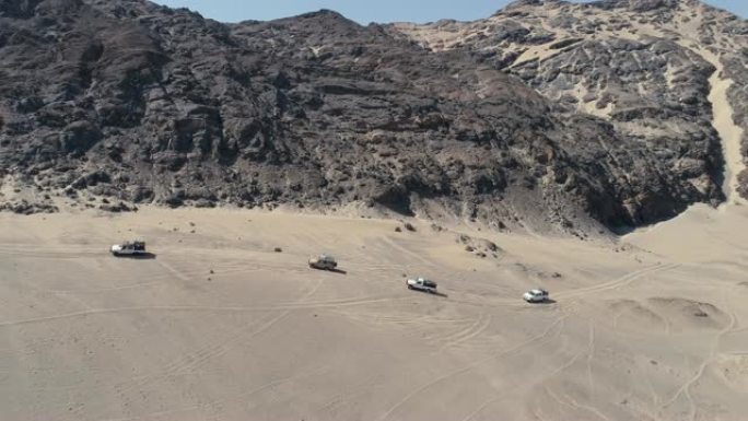 纳米比亚纳米布沙漠骨架海岸上4x4车辆在沙丘和山脉之间行驶的车队的4k空中缩小视图