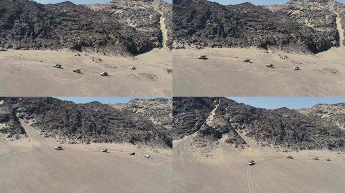 纳米比亚纳米布沙漠骨架海岸上4x4车辆在沙丘和山脉之间行驶的车队的4k空中缩小视图