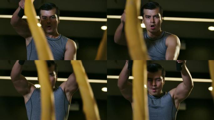 男子在健身房用战斗绳训练。强大的肌肉发达的人在健身房慢动作用绳索进行战斗锻炼。