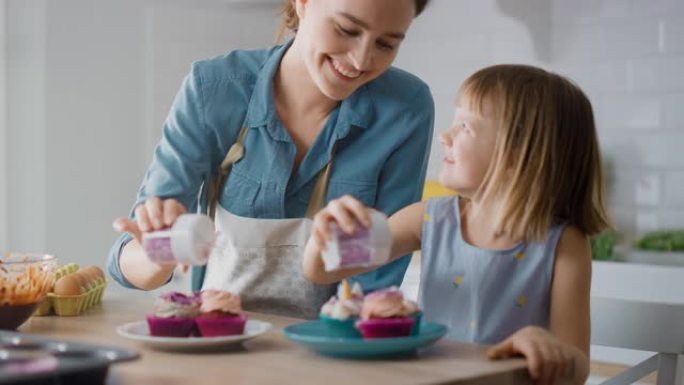 在厨房里: 母亲和可爱的小女儿在奶油蛋糕糖霜上撒上Funfetti。一家人一起煮松饼很开心。可爱的孩