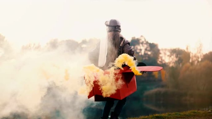 快乐的小女孩扮演飞行员，穿着有趣的飞机服装，彩色烟雾慢动作，在令人惊叹的日落湖周围奔跑。