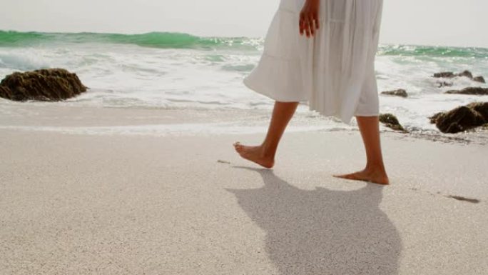 在阳光明媚的日子里，在4k海滩上赤脚行走的女人的低矮部分