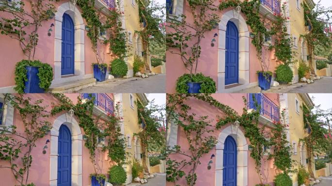 希腊凯法利尼亚岛。房子有柔和的粉色和奶油色的墙壁和蓝色的门，装饰有绿色的植物。起重机射击，4K