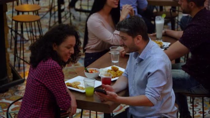 开朗的男人在餐厅用餐时在智能手机上展示一些东西。