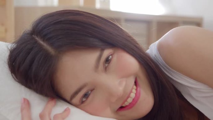 亚洲女人微笑着躺在卧室的床上，美丽的日本女人在家醒来后使用放松时间。生活方式女性使用在家放松时间的概