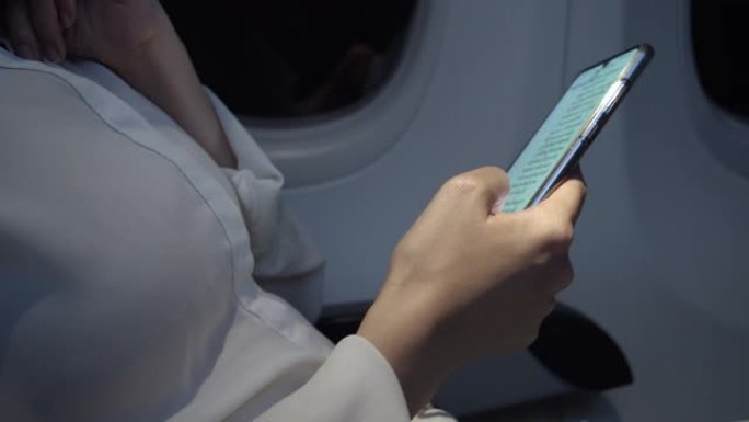 亚洲女性使用智能手机在晚上在飞机上寻找商业计划