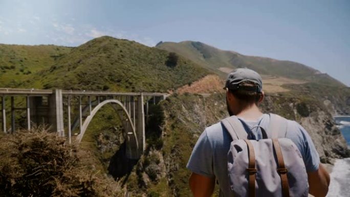 年轻快乐兴奋的旅游男子背着背包看着比克斯比峡谷大桥史诗般的美丽风景，走开。