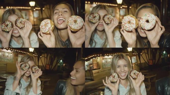肖像的两个可爱的女孩有乐趣做滑稽的脸与甜甜圈的眼睛