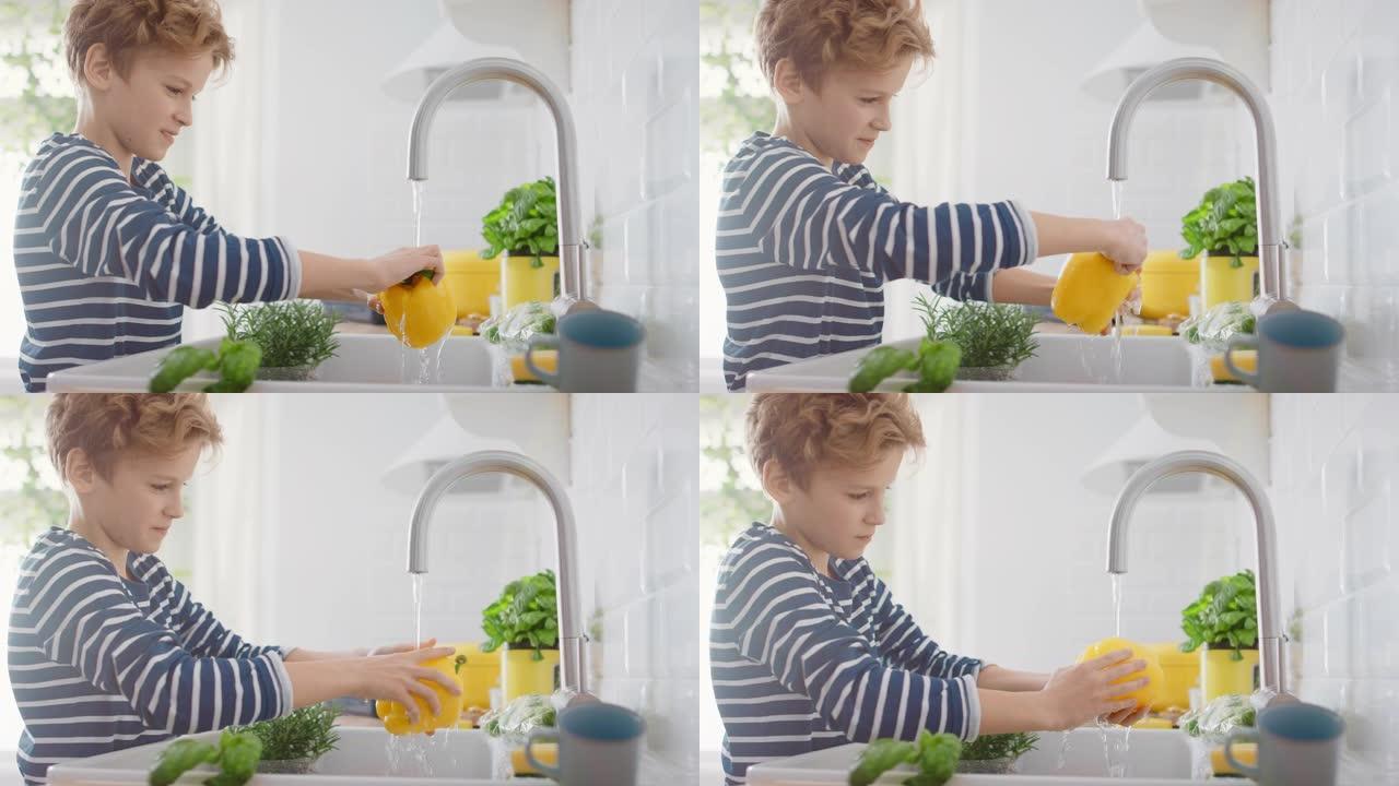 在厨房里: 聪明的小男孩准备沙拉，洗甜椒，其他蔬菜，还有他的手在自来水下的水槽里。小男孩努力做卫生程