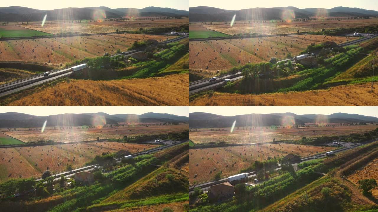 空中无人机镜头: 长途半卡车在意大利农村地区繁忙的高速公路上行驶。背景中的农业作物田和丘陵