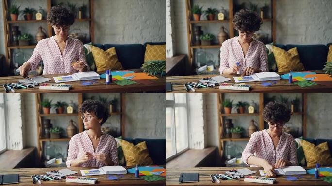 戴眼镜的年轻黑发女人在设计插图时，用胶条和剪刀在笔记本上剪下飞溅纸，然后将人物粘贴在笔记本上。艺术家