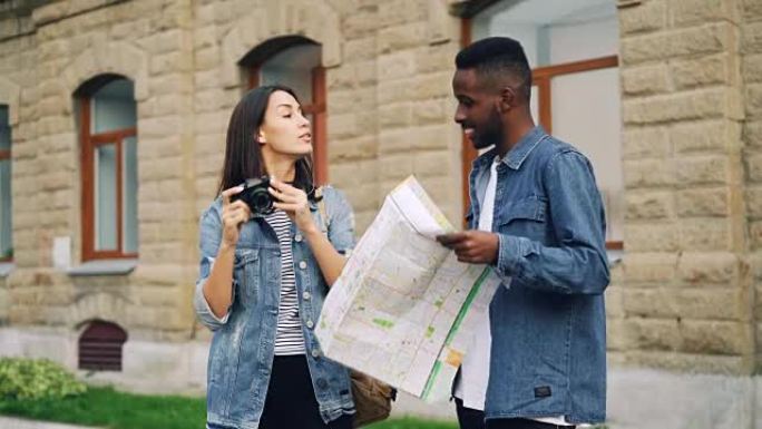 快乐的非洲裔美国人和高加索女孩旅行者正在看地图，站在户外拍照，然后离开。多种族友谊和旅游概念。