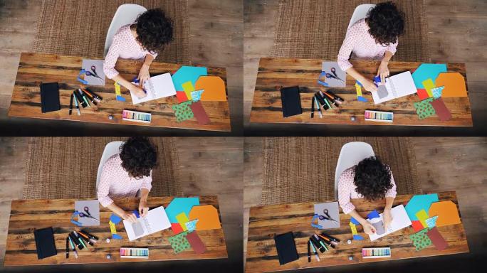 忙碌的女设计师在笔记本上使用胶水粘纸图的俯视图-独自在家工作。创意、设计和现代艺术理念。