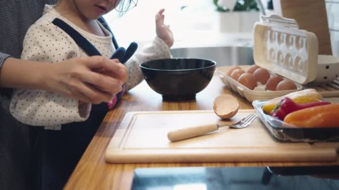 千禧一代的母亲用女儿的帮助手在家做饭煎蛋卷在厨房准备早餐。