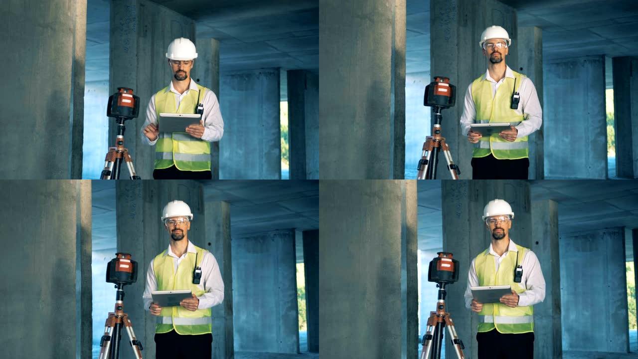 男性建筑检查员正站在土地测量设备附近并在平板电脑上工作