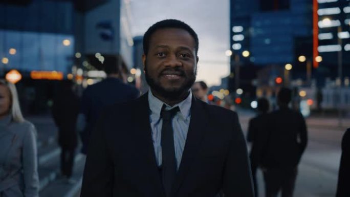 一个穿着西装的非洲裔美国商人的肖像，站在街上，有行人。他看起来很成功，微笑着。今天是傍晚，背景是大气