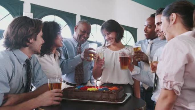 女商人在酒吧与同事一起庆祝生日蛋糕上吹蜡烛