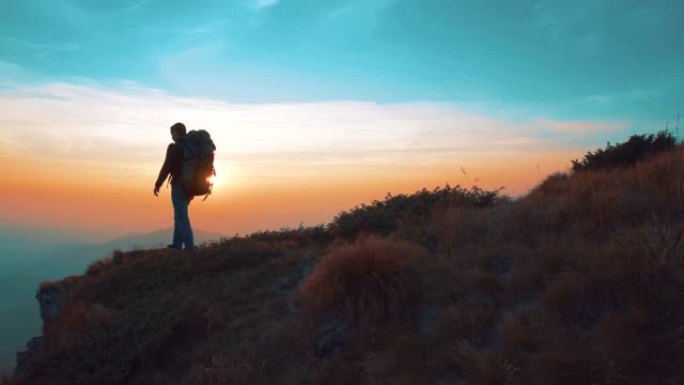 带着旅游背包的男子在日落背景下的山上行走