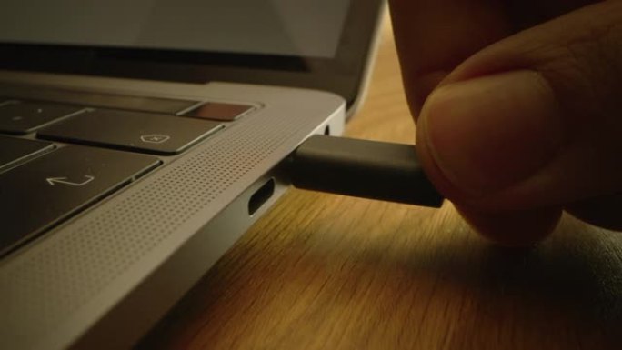 特写微距拍摄: 笔记本电脑放在桌子上，人将usb-c电缆适配器插入计算机端口。