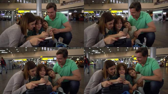 幸福的家庭在机场等待他们的航班，看着智能手机屏幕聊天
