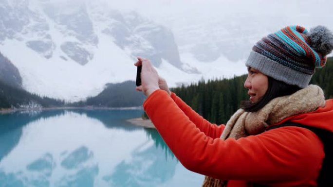 年轻的女旅行者在加拿大艾伯塔省的冰碛湖用智能手机拍照