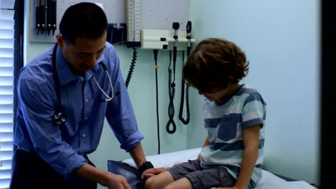 年轻的亚洲男医生在诊所4k检查高加索男孩病人膝盖的前视图