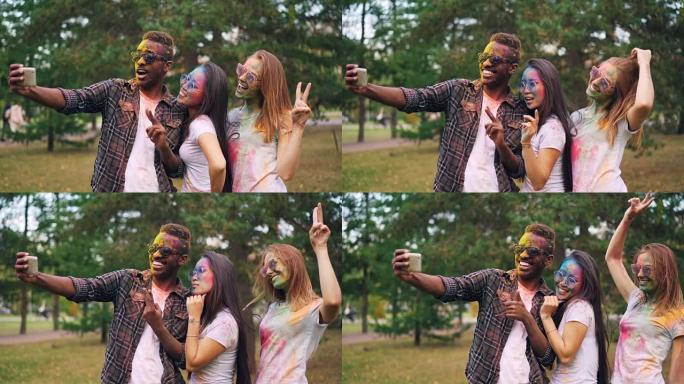 戴着墨镜的非洲裔美国男子的慢动作在洒红节上与漂亮女孩自拍，他们的脸，头发和衣服都被油漆覆盖。