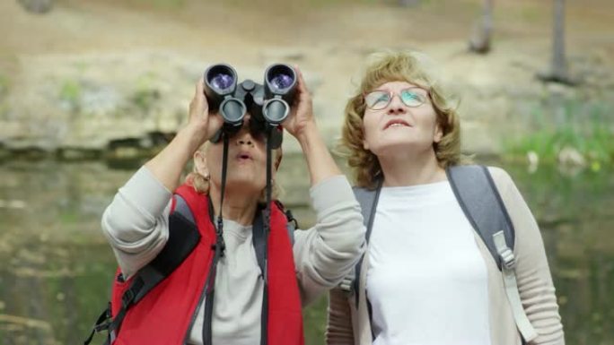 惊讶的高级女性在森林中透过双筒望远镜观看