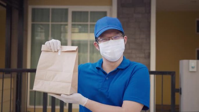 亚洲送货员或邮递员看着相机，微笑着拿着食品纸袋的肖像摆在家门前。统一概念中的送货无接触或无接触送货员